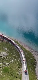 A red train travels by a tranquil blue lake.