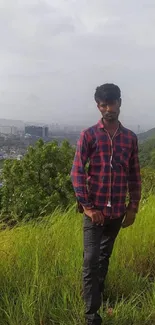 Man standing on grassy hillside with city view in background.