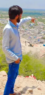 Man pointing towards a distant village landscape from a hilltop.