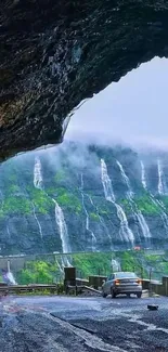 Road with car beside scenic cascading waterfalls on a mountain slope.