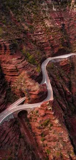 Aerial view of a winding road through a red canyon with cliffs and natural scenery.