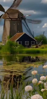 Windmill by a lake with flowers in foreground.