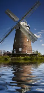 Windmill reflecting on serene waters under a clear blue sky.