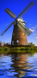 Scenic windmill with mirror-like river reflection under a vibrant blue sky.