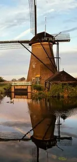 Windmill reflected in calm water under a blue sky.