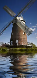 Windmill reflecting on tranquil water under a clear blue sky.