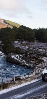 A vehicle drives along a scenic winter road by a river and forest.