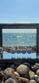 Balanced stones by the sparkling sea under a clear blue sky.