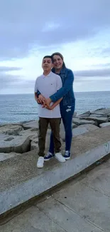 Couple embracing on rocky seaside with clear sky.