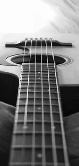 Black and white wallpaper of acoustic guitar on bed with soft lighting.