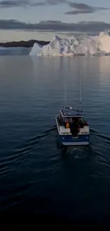 A boat sails through calm blue waters in front of large Arctic icebergs.