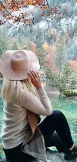 Woman sits by a tranquil autumn lake surrounded by colorful trees.