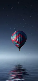 Colorful hot air balloon floats over calm water under a starry sky.