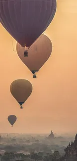 Hot air balloons float over misty landscape at sunset.