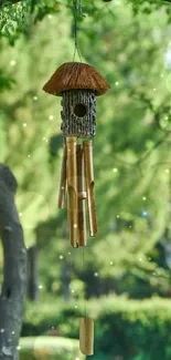 Bamboo wind chime hanging among green trees in a serene outdoor setting.