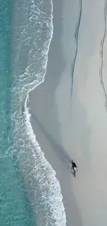 Aerial view of a beach with a lone person, waves, and soft sand.