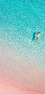 Aerial view of person floating in turquoise water near pink sand beach.