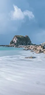 Serene beach with rocky island under calm sky.