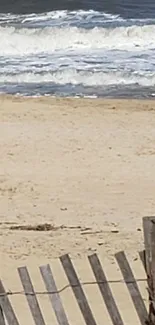 Serene beach view with a rustic fence along sandy shores and gentle ocean waves.