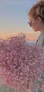 Woman with pink flowers by beach at sunset.