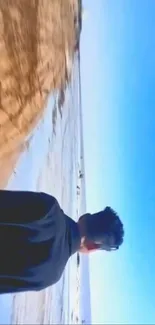 Man overlooking ocean on a serene beach with clear blue sky.