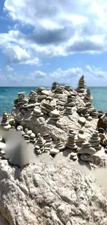 Stacked rock cairns on a serene beach with ocean and sky backdrop.