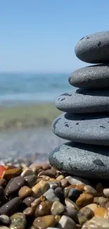 Balanced stones on a peaceful pebble beach with ocean and blue sky backdrop.