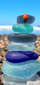 Stacked sea glass and ladybug on beach.