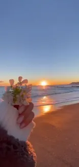 Serene sunset over a beach with a hand holding flowers.