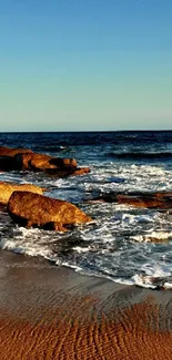 Beautiful sunset view of ocean waves on a sandy beach with rocks.