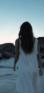 Woman walking on a serene beach at dusk.