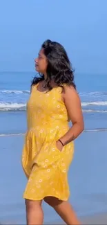 Woman in yellow dress walking on beach with waves in background.