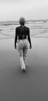 Person walking along a serene beach in grayscale.