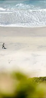 A person walking along a tranquil beach with waves in the distance.