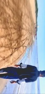 Person walking on a tranquil beach with the ocean and sky view.