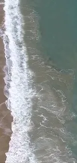 Aerial view of turquoise ocean waves gently lapping onto a sandy beach shore.