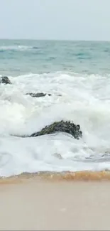 Peaceful beach with foamy waves crashing on rocks and sand.