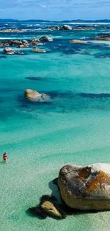 Turquoise sea with rocks and a person on a serene beach.