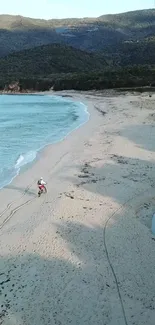 Two riders on a deserted beach with mountains in the background.