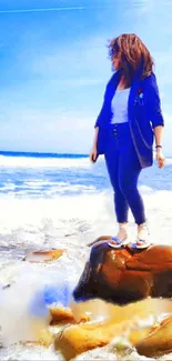 Woman stands on rock by ocean under a clear blue sky.