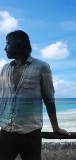 Man stands by railing overlooking serene beach and ocean under a blue sky.