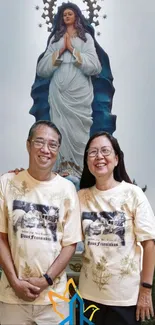 Couple standing before Virgin Mary statue in serene mobile wallpaper.