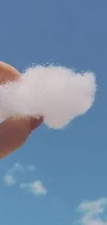 Hand holding cloud against a blue sky.