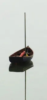 A solitary wooden boat reflected on calm, light gray water.