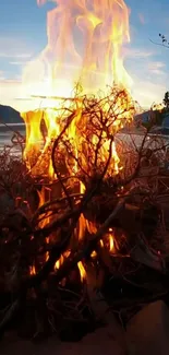 Campfire at sunset by a tranquil lake with vibrant flames.