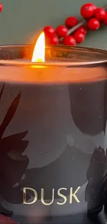 Lit dusk candle with red berries and pinecone on a serene winter background.