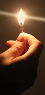 A hand holding a lit matchstick in the dark.