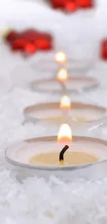 Lit candles on a snowy surface with red decorations in the background.