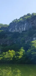 Majestic cliff reflected in calm lake with lush greenery.