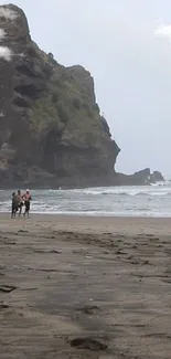 People walking on a serene beach with towering rock formations.